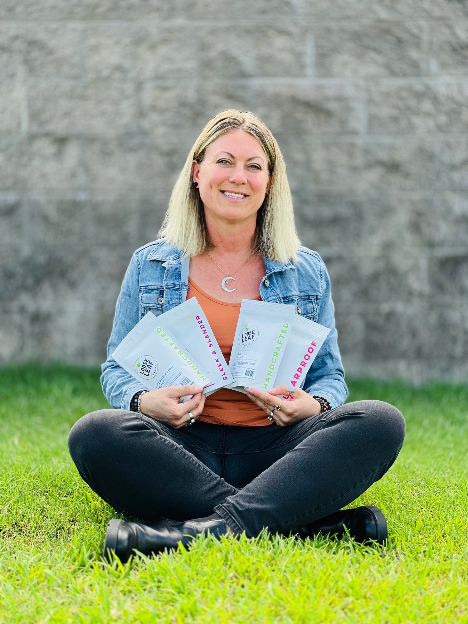 Woman sitting in the grass holding four bags of Loose Leaf Tea.