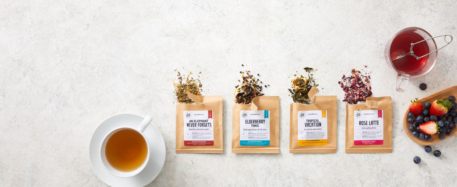 Samples of loose leaf tea on a counter with a cup of tea and fresh fruit