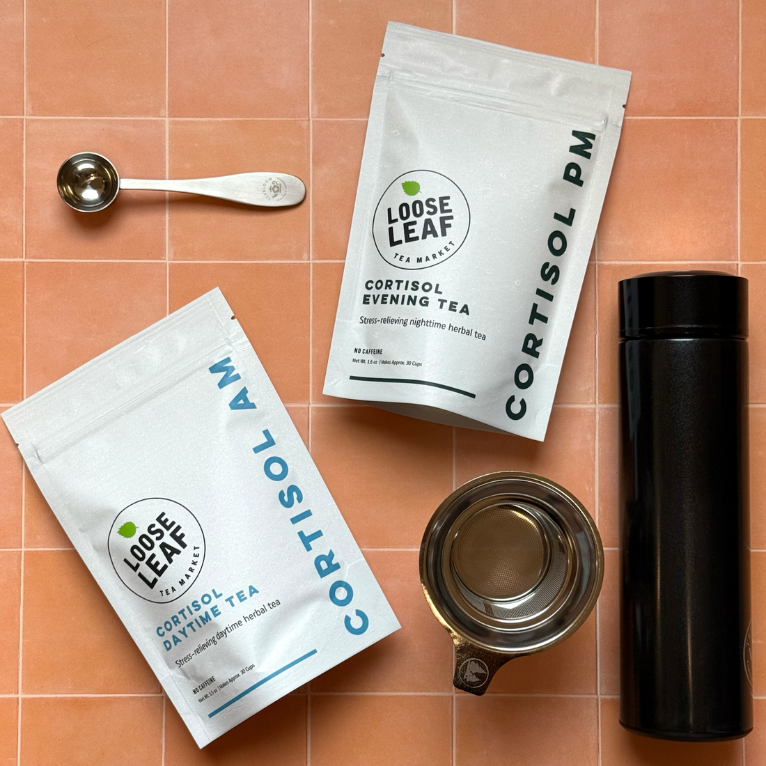 The two teas in the Cortisol Tea Bundle with a stainless steel tea scoop, stainless steel tea infuser, and travel tea tumbler.