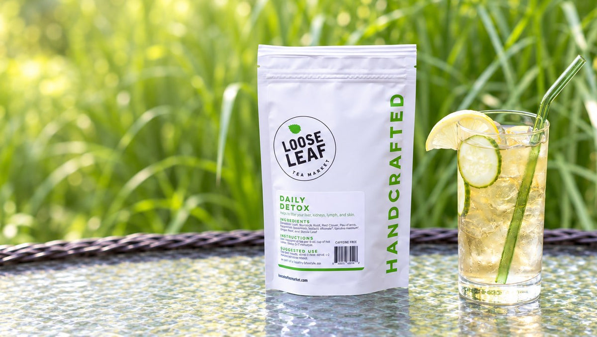 Loose Leaf Tea Market Daily Detox pouch beside a glass of iced tea with lemon and cucumber on a garden table
