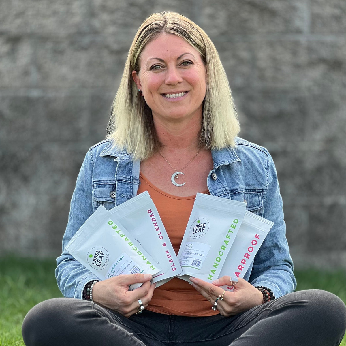 Woman sitting on the grass holding four Loose Leaf Tea Market tea pouches